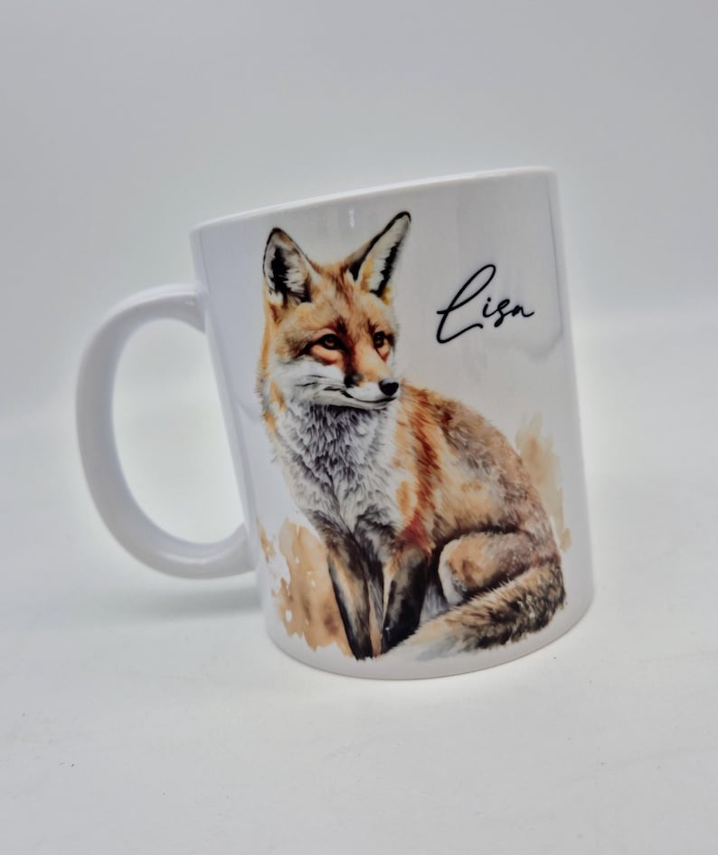 May include: White ceramic mug featuring a watercolor illustration of a fox in shades of brown, orange, and white. The mug has a curved handle and the name "Lisa" in black script.