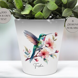 May include: White ceramic plant pot with a watercolour hummingbird design on a flowering branch. The pot has the name "Tasha" and two circular labels that read "Add your own text" and "8 designs available".
