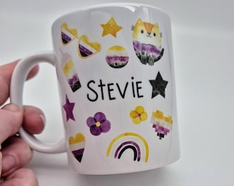May include: White ceramic mug with a black and white cat design, a rainbow, stars, hearts, and flowers. The mug has the name "Stevie" written on it.