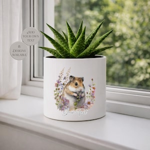 May include: White ceramic planter with a watercolor illustration of a hamster surrounded by flowers. The planter holds a green aloe vera plant. Text on the planter reads "Add Your Own Text" and "8 Designs Available".