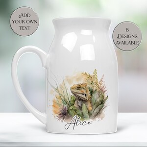Peut inclure: Mug en céramique blanche avec une grande anse, orné d'une illustration à l'aquarelle d'un dragon barbu au milieu de la verdure. La tasse porte le nom "Alice". Le texte "Add Your Own Text" et "8 Designs Available" sont également visibles.