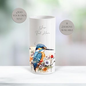 Könnte beinhalten: Eine weiße zylindrische Vase mit einer Aquarellillustration eines Eisvogels mit blauen und orangefarbenen Federn, umgeben von Blumen. Auf der Vase steht der Text "Your Text Here", "Add Your Own Text" und "8 Designs Available".
