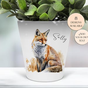 May include: White ceramic plant pot with a watercolour illustration of a fox in shades of orange and brown. The pot has the name "Sally" in script and two circular labels: "8 Designs Available" and "Add Your Own Text".