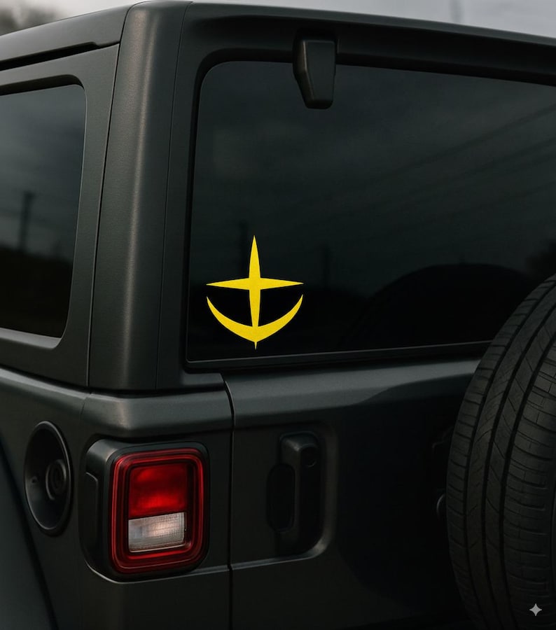 Puede incluir: Una pegatina amarilla con un dise&ntilde;o de ancla estilizada con una cruz en la parte superior, adherida a la ventana trasera de un SUV negro. La pegatina tiene un dise&ntilde;o gr&aacute;fico simple. La luz trasera del veh&iacute;culo es visible.
