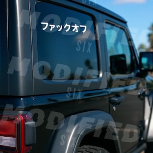 a black Jeep Wrangler parked outdoors, with a sticker on the rear window that says "Six".