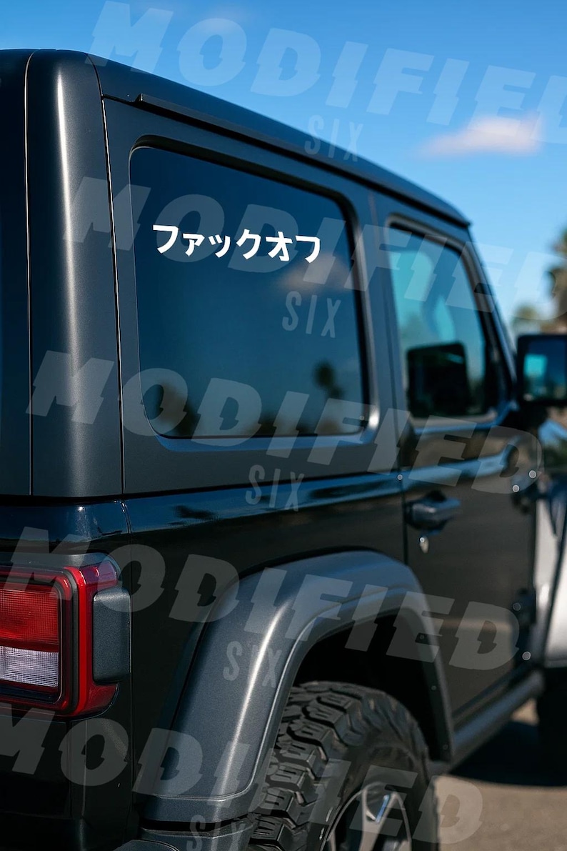 a black Jeep Wrangler parked outdoors, with a sticker on the rear window that says "Six".
