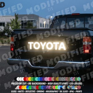 May include: Black Toyota truck with a reflective "TOYOTA" decal on the tailgate. The image shows the truck's rear, with the text illuminated. The bottom of the image displays a color palette of vinyl options.