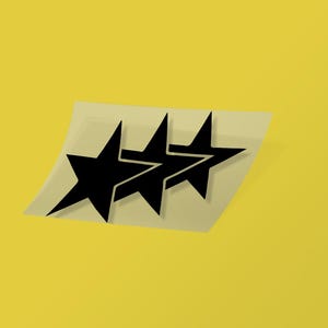 May include: Three black star-shaped decals on a light-colored backing, set against a yellow background. The stars have sharp points and are arranged in a row. The decals appear to be stickers or transfers.
