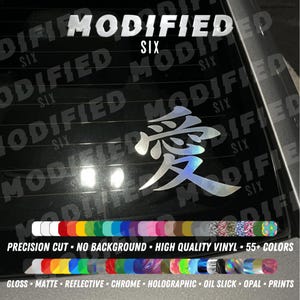 Puede incluir: Una calcomanía de vinilo holográfico con el carácter kanji japonés para el amor, aplicada sobre una superficie de vidrio oscuro. La imagen incluye superposiciones de texto MODIFIED SIX, junto con dos filas de muestras de color y etiquetas.