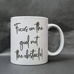 May include: A silver glitter mug with the text "Focus on the goal not the obstacle!" printed in black.