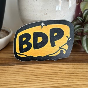 May include: A yellow and black sticker with the text "BDP" in a speech bubble shape.