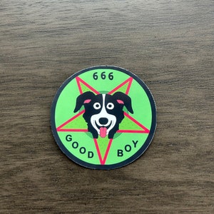 May include: A green and red circular sticker with a black and white dog illustration inside a pentagram. The text "666 GOOD BOY" is written around the pentagram.