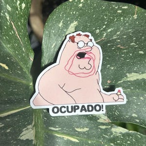 May include: A sticker depicting a cartoon character with glasses and a surprised expression. The character is nude, with a pink outline. The text "OCUPADO!" is printed in black on a white background.