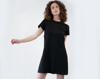 May include: A woman wearing a black short-sleeved t-shirt dress with grey socks and black shoes.