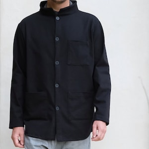 May include: A black long-sleeved shirt with a mandarin collar and button closure. The shirt has two chest pockets and two lower pockets. The model is wearing gray pants.