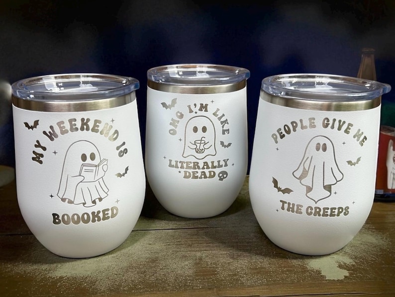May include: Three white insulated wine tumblers with silver rims and lids. Each tumbler features a ghost graphic and text: "My Weekend Is Boooked", "OMG I'm Like Literally Dead", and "People Give Me The Creeps". Bats are also included in the design.