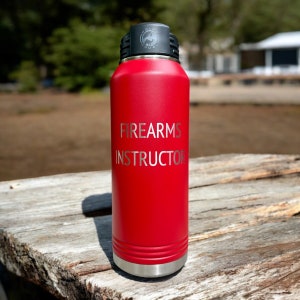 May include: Red insulated water bottle with a black lid and a silver base. The bottle has the words "FIREARMS INSTRUCTOR" engraved on the side.