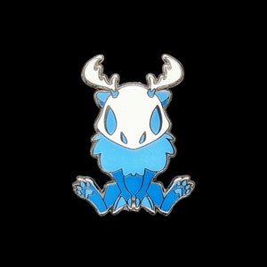Pu&ograve; includere: Spilla in smalto blu e bianco raffigurante un personaggio dei cartoni animati con corna, petto soffice e in posizione seduta. La spilla ha un contorno argentato su sfondo nero.