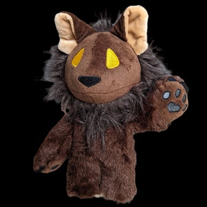 May include: A brown plush lion with a long mane, yellow eyes, and a black nose. The lion has a paw print on one hand.