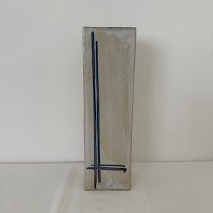 Könnte beinhalten: Eine hohe, weiße Keramikvase mit einem einfachen, abstrakten Design aus schwarzen Linien.