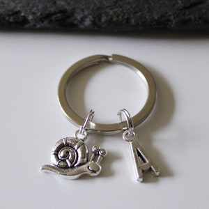 Könnte beinhalten: Silberner Schlüsselanhänger mit einem Schnecken-Anhänger und einem Buchstaben A-Anhänger.