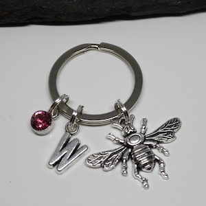 May include: A silver keychain with a pink rhinestone, a silver letter W charm, and a silver bee charm.