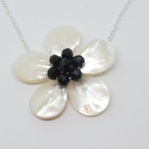 May include: A silver chain necklace with a white mother of pearl flower pendant. The flower has a centre of black crystal beads.