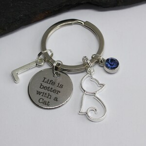 Peut inclure: Porte-clés argenté avec un charme qui dit "La vie est meilleure avec un chat" et un petit charme de chat. Le porte-clés a également un charme de cristal bleu et un charme de lettre L argenté.