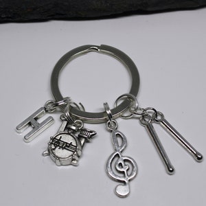May include: Silver keychain with a drum, a treble clef, two drumsticks, and the letter H.