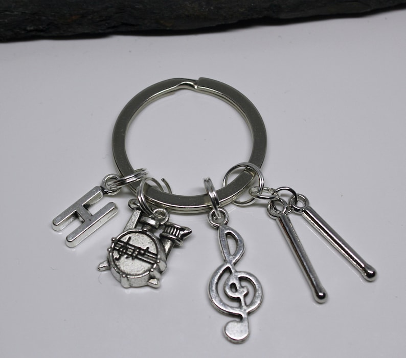 May include: Silver keychain with a drum, a treble clef, two drumsticks, and the letter H.
