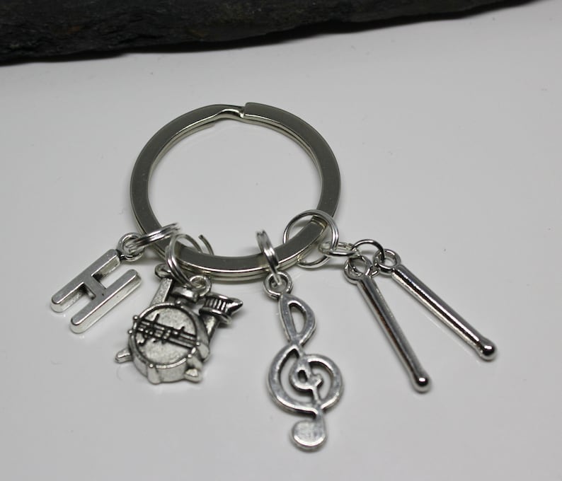 May include: Silver keychain with a variety of charms, including a drum, a treble clef, drumsticks, and the letter H.