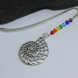 Puede incluir: Marcapáginas de plata con un amuleto de cristal arcoíris y un colgante de concha espiral plateada.