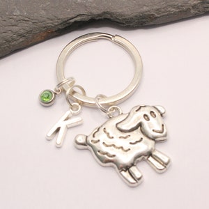 May include: Silver keyring with a charm of a sheep, a letter K charm, and a green gemstone.