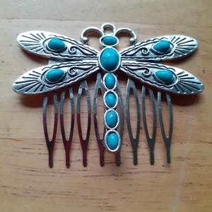 Puede incluir: Peine para el cabello de libélula plateado con acentos de piedras preciosas azul turquesa. El peine tiene un diseño decorativo y siete dientes.