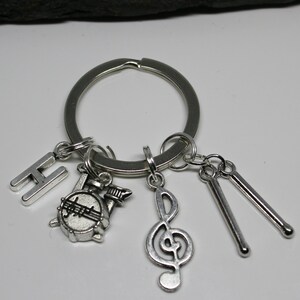 May include: Silver keychain with a silver letter H, a silver drum, a silver treble clef, and two silver drumsticks.