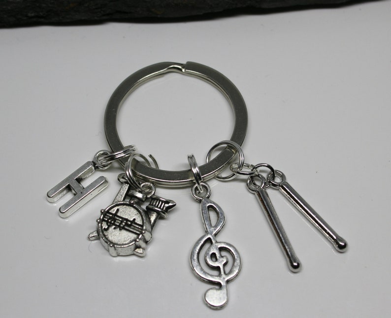 May include: Silver keychain with a silver letter H, a silver drum, a silver treble clef, and two silver drumsticks.
