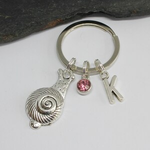 Peut inclure: Porte-clés en argent avec un charme d'escargot, un strass rose et un charme en argent avec la lettre K.