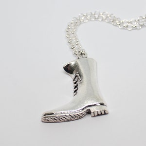 Puede incluir: Collar con colgante de bota plateada. El colgante es una miniatura detallada de una bota de trabajo, con cordones y suela texturizada. La cadena del collar es plateada, y el colgante de la bota mide unos 4 cm de altura.