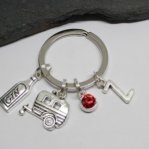 May include: Silver keychain with a charm of a caravan, a bottle with the word "GIN" on it, a red rhinestone, and the number "7".