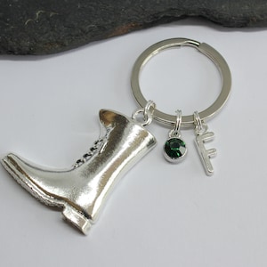 Może przedstawiać: Brelok do kluczy w kształcie srebrnej botki z zielonym kamieniem szlachetnym i srebrnym zawieszką z literą F.