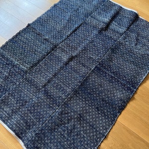 May include: A dark blue rug with a white diamond pattern. The rug is made of woven fabric and has a fringed edge.