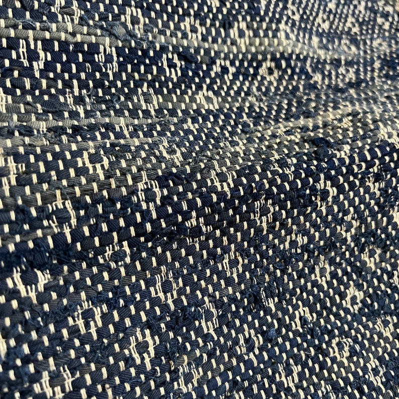 May include: Close-up of a woven rug with a blue and white pattern. The rug is made of thick, textured yarn and has a slightly uneven surface.
