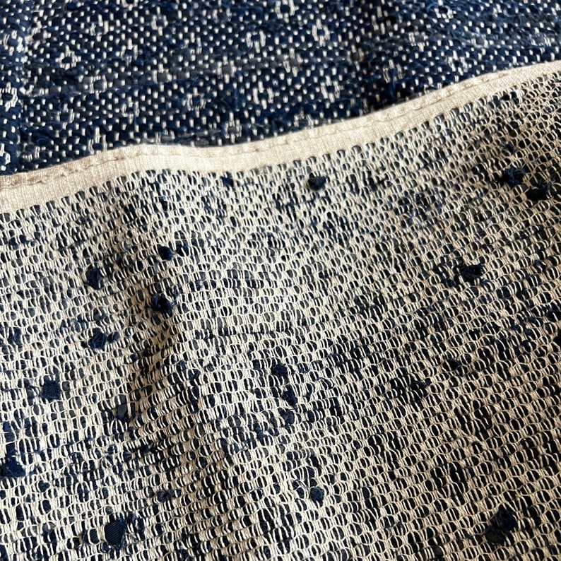 May include: Close-up of a woven fabric with a white background and black woven threads. The fabric has a textured, almost bumpy surface.