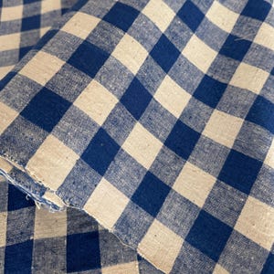 Peut inclure: Gros plan sur un tissu à carreaux bleu et blanc. Le tissu présente un motif vichy classique avec des carrés bleus et blancs alternés. Le tissu semble être plié, montrant plusieurs couches de matière.