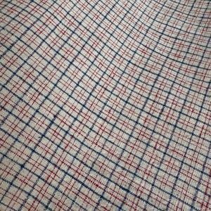 May include: A woven fabric featuring a grid pattern with dark blue lines intersecting on a light beige background, accented by thin, dashed red lines running horizontally and vertically through the centre of each square in the grid design.
