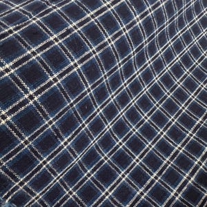 Pode incluir: Close-up de um tecido xadrez azul marinho e branco. O tecido tem uma textura tecida com um padrão de grade de linhas brancas sobre um fundo azul escuro. O design xadrez é composto por quadrados e retângulos.