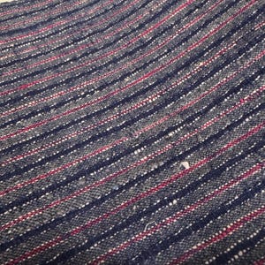 Peut inclure: Un tissu textile tissé présentant un motif texturé de rayures diagonales en bleu marine foncé, gris anthracite, blanc et magenta. Le matériau présente un tissage grossier visible avec de petites taches de fibres plus claires dispersées.