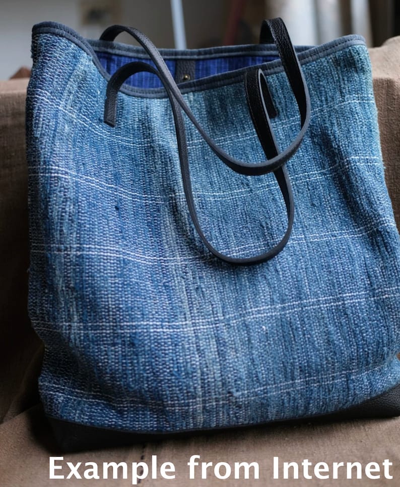 May include: A blue denim tote bag with black leather straps and a woven texture. The bag has a simple design and is made of durable material.