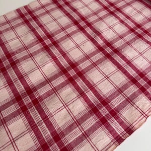 Pode incluir: Um tecido xadrez vermelho e branco com um padrão clássico. O tecido apresenta uma grade de linhas que se cruzam em uma cor vermelha vibrante contra um fundo branco. O tecido é provavelmente algodão ou linho.