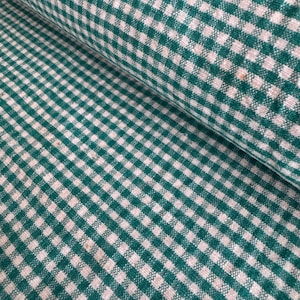 Può includere: Un rotolo di tessuto a quadri verdi e bianchi. Il tessuto presenta un classico motivo a quadretti, con piccoli quadrati uniformemente distanziati. Il tessuto è a trama fitta e sembra essere realizzato in cotone o materiale simile. Il tessuto è piegato.